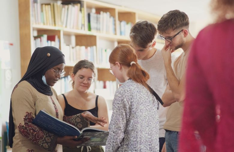 Eine Gruppe von Jugendlichen blickt gemeinsam in ein Buch, welches eine Teilnehmerin hält.