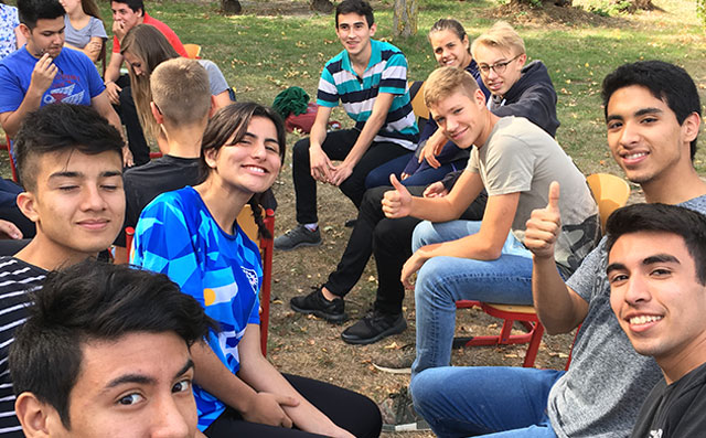 Eine Gruppe Jugendlicher sitzt draußen zusammen und sie lachen in die Kamera.