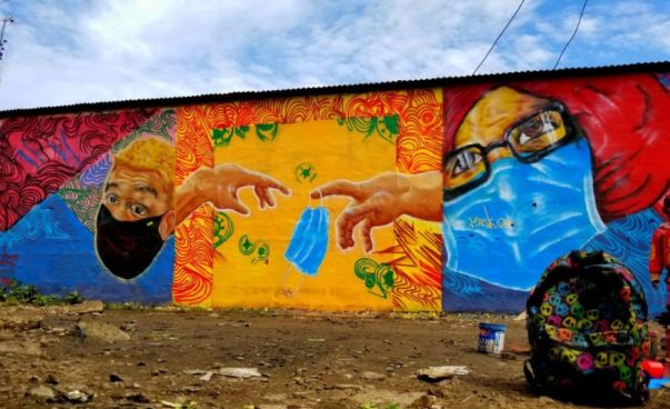 Eine Wand, mit einem Graffiti, rechts und links sind Menschen mit medizinischer Maske abgebildet, in der Mitte ein parodistischer Ausschnitt aus „Adams Erschaffung“, an einem der Finger hängt eine medizinische Mask. Foto: Shaffie Abdi