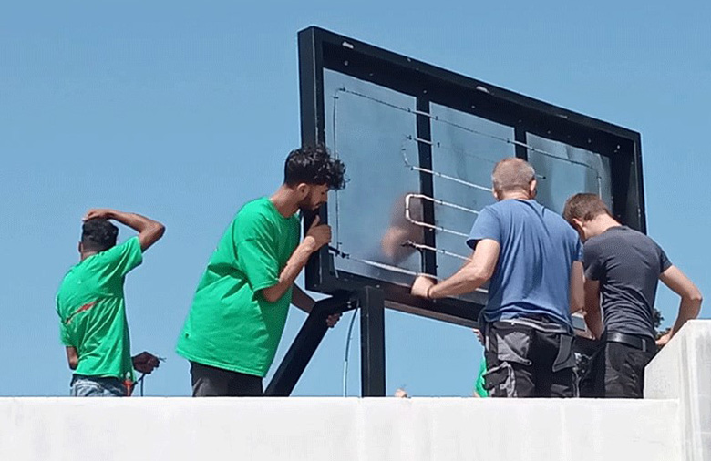 Vier Menschen arbeiten an der Werbetafel auf dem Dach.